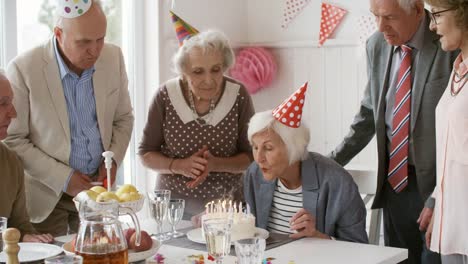 Elderly-Woman-Blowing-Off-Candles-at-Birthday-Party-with-Friends