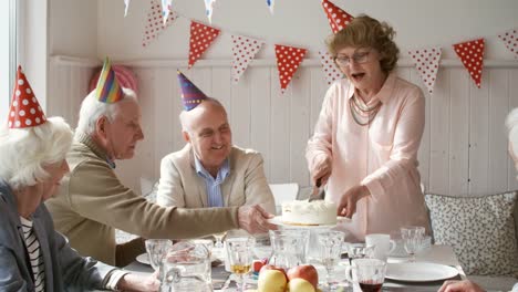 Happy-Senior-Woman-Cutting-Geburtstagskuchen-für-Gäste