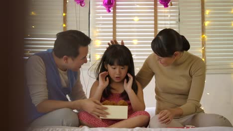 Happy-asian-family-celebrating-daughter's-birthday-opening-gifts-and-rejoice-on-bed.-Christmas,-happy-birthday-celebration.-New-Year-party.-Slow-motion.