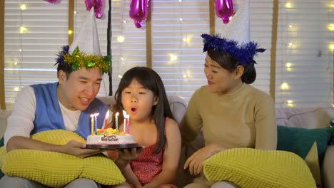 Eine-niedliche-kleine-asiatische-Mädchen-feiern-ihren-Geburtstag-mit-einer-Torte-und-glückliche-Familie.-Sie-gibt-ein-breites-Lächeln-und-ihre-Familie-begrüßen-sie.-In-Zeitlupe.