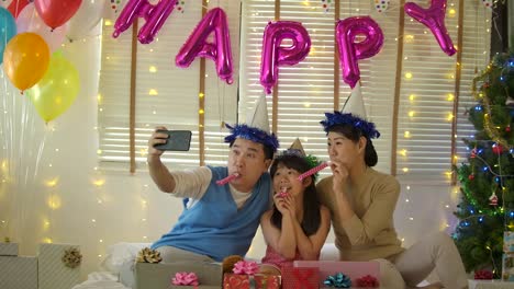 Best-time-together.-Happy-young-family-sitting-on-the-bed-and-blowing-party-horn-blowers-while-all-of-them-wearing-party-hats-in-Slow-motion.