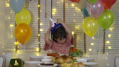 Sad-little-asian-girl-celebrating-her-birthday-alone-at-a-table-with-a-cake-and-a-candle,-Guests-do-not-come.-Slow-motion.