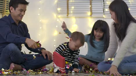 Happy-asian-family-sitting-on-floor-in-living-room-and-playing-with-confetti-in-slow-motion.