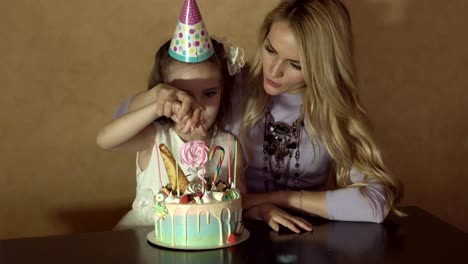 mother-and-daughter-countIng-candles-on-a-birthday-cake.-little-girl-in-a-festive-hat-at-a-children's-party