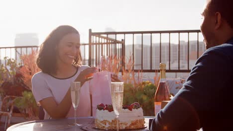 Mann-Frau-Geschenk-und-Karte-zu-geben,-wie-sie-auf-Dachterrasse-mit-Skyline-der-Stadt-im-Hintergrund-feiern