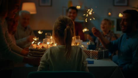 Back-View-Shot:-Birthday-Celebration-of-Cute-Little-Girl-at-the-Dinner-Table,-Mother-Brings-Cake-and-Girl-Blows-Out-Candles.-At-the-Table-Happy-Relatives-and-Friends-Gathered-To-Celebrate.