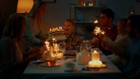 Birthday-Celebration-of-Cute-Little-Girl-at-the-Dinner-Table,-Mother-Brings-Cake-and-Girl-Blows-Out-Candles.-At-the-Table-Happy-Relatives-and-Friends-Gathered-To-Celebrate.