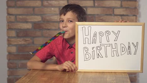 niño-sentado-en-el-escritorio-con-rotafolio-con-letras-feliz-cumpleaños-en-el-muro-de-ladrillo-rojo-de-fondo