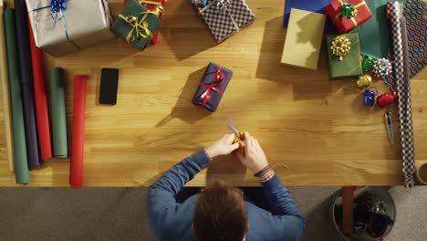 Top-View-of-Young-Man-Skillfully-Packing-Colorful-Gifts-in-His-Sunny-Studio.