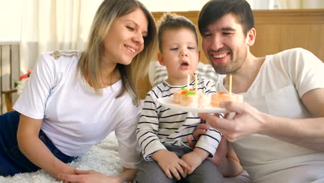 Familia-sonriente-celebrando-su-cumpleaños-hijo-juntos-y-soplando-velas-en-el-pastel