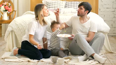 Kleine-entzückende-Junge-feiert-seinen-Geburtstag-mit-Vater-und-Mutter-essen-Kuchen-im-Schlafzimmer