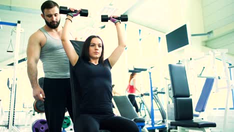 Trainer-helps-young-strong-brunette-woman-doing-exercise-in-fitness-club-and-gym-center