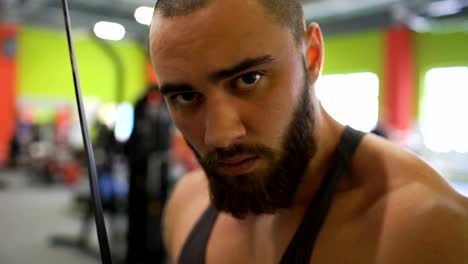 Handsome-sporty-man-is-exercising-looking-into-camera-in-fitness-club