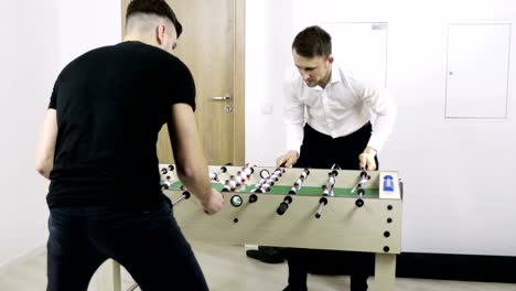 Two-young-men-play-table-soccer-in-the-office.