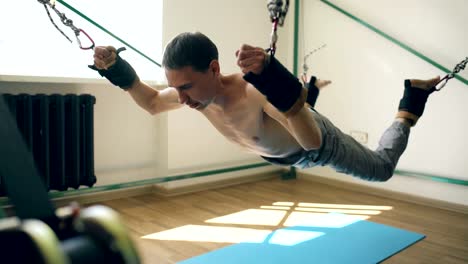 Young-man-doing-exircise-on-quartering-gym-equipment-and-pull-his-arms-and-legs-with-ropes