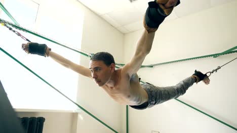 Young-man-doing-exircise-on-quartering-yoga-equipment-and-pull-his-arms-and-legs-with-ropes