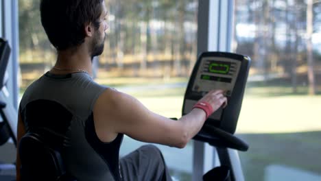 Handsome-fit-sporty-man-is-exercising-on-stationary-cardio-bicycle-in-the-gym.