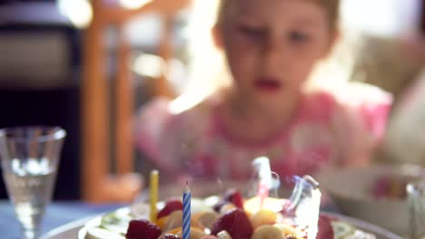 Niña-sopla-las-velas-en-el-pastel-de-cumpleaños-y-claping-sus-manos