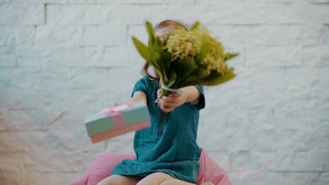 niedliche-kleine-Mädchen-zeigt-Blumen-und-ein-Geschenk