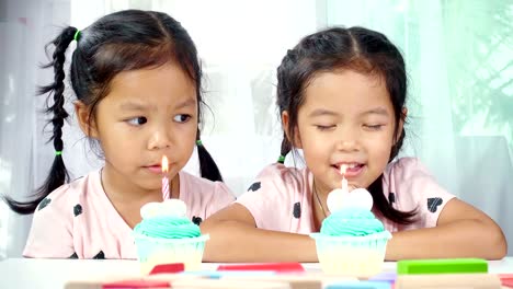 Two-asian-little-girl-blows-out-candles-on-birthday-cake-together-in-house