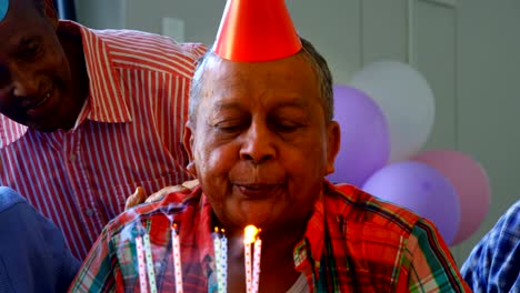 Senior-man-blowing-out-the-candles-on-a-birthday-cake-with-his-friends-4k