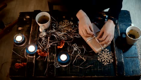 Close-up-Draufsicht-des-weiblichen-Händen-Geschenk-am-Tisch-zu-Hause.-Frau-bindet-eine-Weihnachts-Box-mit-einem-Band