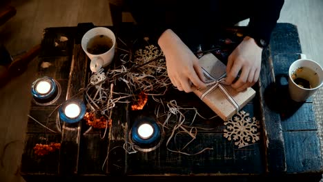 Vista-de-la-mujer-sentada-a-la-mesa-con-decoración-de-personal-superior-y-haciendo-el-presente,-una-caja-de-Navidad-con-una-cinta-de-lazo