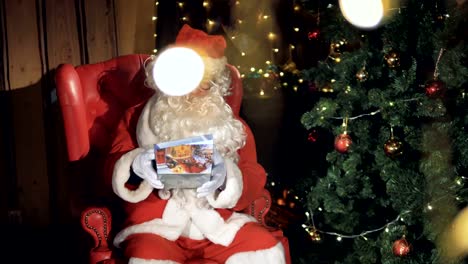 Santa-Claus-packing-a-gift-box-sitting-in-a-chair-near-christmas-tree.