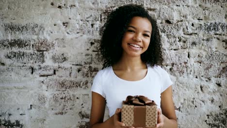 Portrait-of-young-african-american-woman-holding-gift-box-and-smiling-into-camera