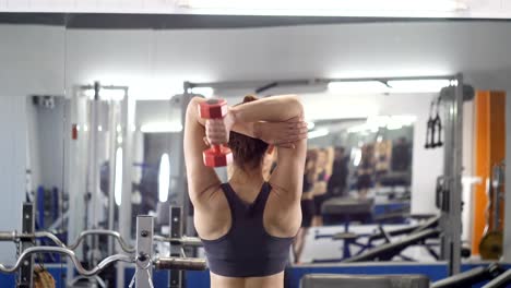 Deportes-niña-haciendo-ejercicio-de-extensión-de-tríceps-en-gimnasio.-Mujer-sosteniendo-peso-libre-en-las-manos-a-la-cabeza,-luego-lo-disminuye.-Vista-de-la-parte-posterior.-60-fps