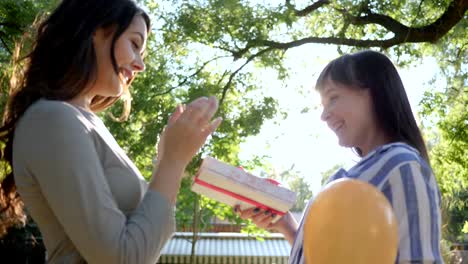 girl-with-colorful-balloons-giving-presents-and-hugging-girlfriend-outdoors-in-park,-emotions