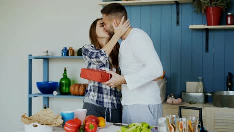 Risa-a-mujer-atractiva-sorprendente-su-boylfriend-con-un-regalo-en-su-casa-en-la-cocina-mientras-se-cocina-el-desayuno