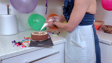 Woman-decorate-cake-with-culinary-syringe-in-kitchen