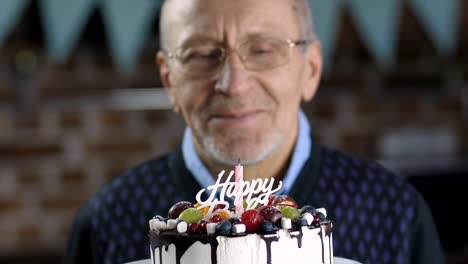 Close-up-of-senior-man-blowing-candle-on-cake