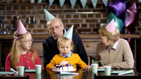 Muchacho-que-sopla-velas-sobre-el-pastel-con-sus-abuelos