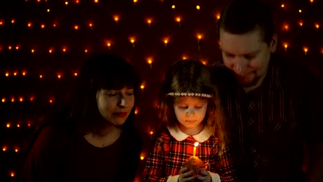 A-little-girl-blows-out-a-candle-on-a-festive-cake-with-her-mom-and-dad.