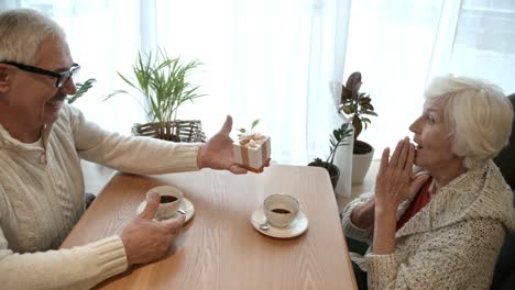 Senior-hombre-dar-regalo-a-esposa-en-fecha-en-cafetería