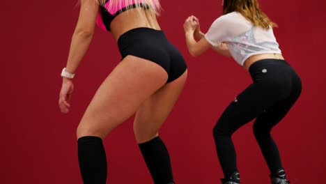 A-beautiful-sexy-girl-on-a-red-wall-background-performs-squats-to-strengthen-the-thigh-muscles.-Training-of-gluteal-muscles-in-boots-on-springs.-Sports-shoes-exercise