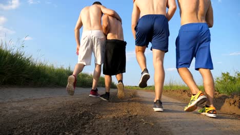 Male-friends-walking-on-country-road-and-having-fun.-Group-of-happy-boys-fool-around-outdoors.-Rear-back-view-Low-angle-view-Close-up