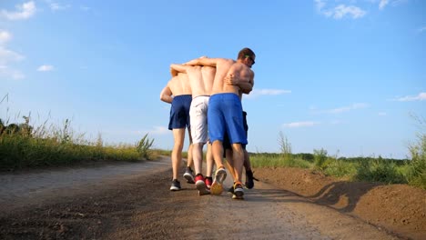 Male-friends-walking-on-country-road-and-having-fun.-Group-of-happy-boys-fool-around-outdoors.-Rear-back-view-Low-angle-view-Close-up