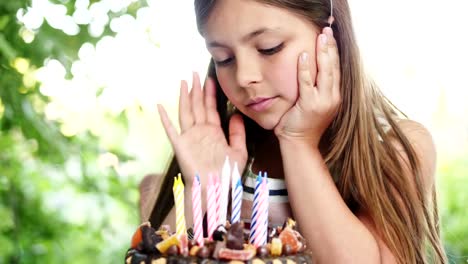 Glückliches-Mädchen-am-Tisch-im-Garten-sitzen-und-bewundert-eine-festliche-Torte