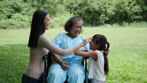 Grandmother-sitting-on-wheelchair-with-daughter-and-granddaughter-enjoy-in-the-park-together