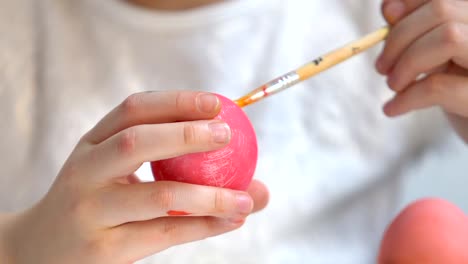 Little-kid-using-brush-with-yellow-paint-to-decorate-dyed-Easter-egg,-creativity