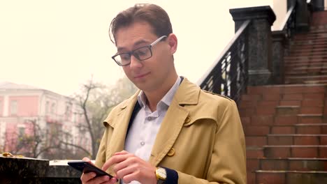 Closeup-portrait-of-attractive-caucasian-man-browsing-on-his-phone-and-standing-in-the-park-outdoors