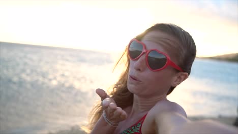 Junge-Frau-trägt-Herz-geformt-rote-Sonnenbrille-Selfie-Aufnahme-bei-Sonnenuntergang-am-schönen-Strand-von-Hawaii.-Slow-motion