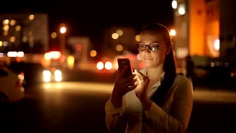 Porträt-der-jungen-schönen-kaukasischen-Frau-mit-Smart-Phone-Hand-halten-im-Freien-in-der-Stadtnacht,-lächelnd,-Gesicht-beleuchteten-Bildschirmlicht-soziales-Netzwerk,-Technologie,-Kommunikation-Konzept