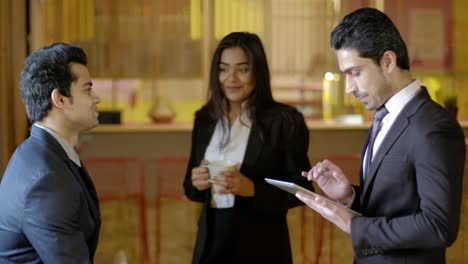 Young-Indian-coworkers-at-a-cool-edgy-co-working-place--have-an-engaging-and--informal-discussion-talk-in-the-morning-at-the-breakout-area-with-a-tea-and-a-tablet