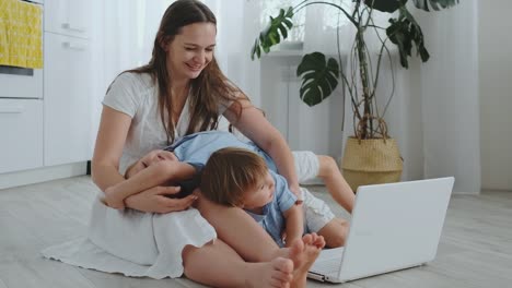 Schöne-moderne-junge-Familie-liegt-zu-Hause-auf-dem-Boden-und-macht-etwas-im-Laptop