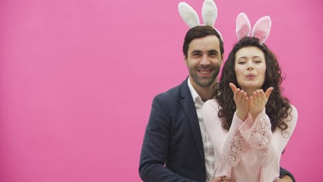 Young-couple-hugging-on-a-pink-background.-During-this-time,-they-look-at-the-camera-together,-the-girl-sends-an-air-kiss.-Sincerely-smile.