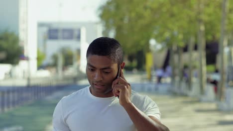 Nachdenklicher-muskulöser-Sportler-im-Gespräch-auf-Smartphone-im-Freien.